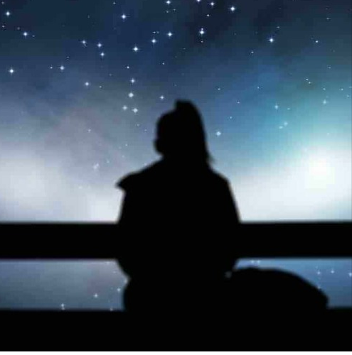 femme assise de dos contemplant la nuit étoilée